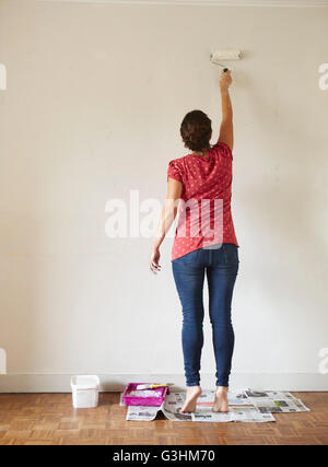 Woman painting wall using paint roller, rear view Stock Photo