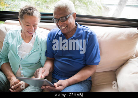 Senior couple sitting on sofa, using digital tablet Stock Photo