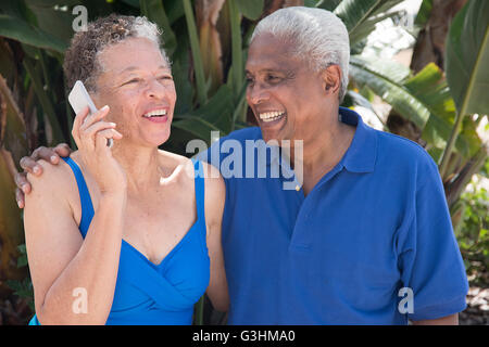 Senior couple sitting outdoors, using smartphone, smiling Stock Photo