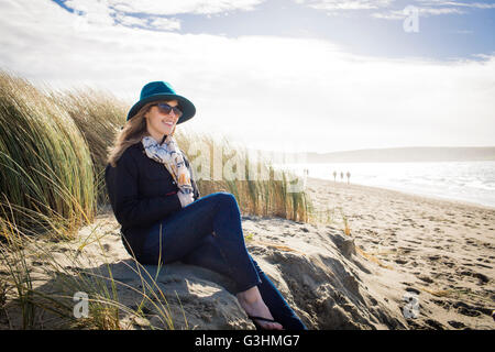 Woman wearing felt hat and sunglasses sitting on dunes, Dillon Beach, California, USA Stock Photo