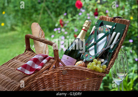 PICNIC HAMPER English sparkling Rosé wine bottle and wicker picnic basket in sunny floral garden situation Stock Photo