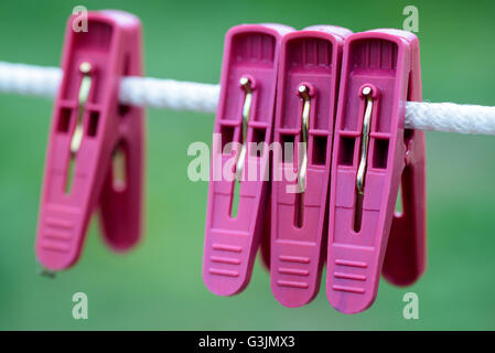 Red plastic domestic washing pegs on a white rope washing line outdoors Stock Photo