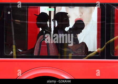 A view of three men sitting in a red London bus - an advertisement on another red London bus in the background Stock Photo