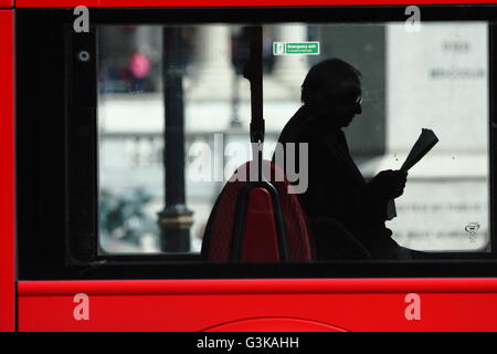 A view of a male reading a newspaper while sitting inside a red London bus in Trafalgar Square, London, England. Stock Photo