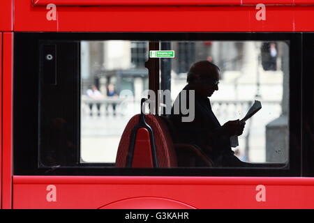 A view of a male reading a newspaper while sitting inside a red London bus in Trafalgar Square, London, England. Stock Photo