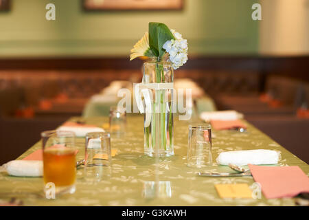 A small glass vase of white flowers on a green table at a wedding reception. Stock Photo