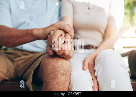 Close up shot of senior couple holding hand. Loving couple sitting together and holding hands. Focus on hands. Stock Photo
