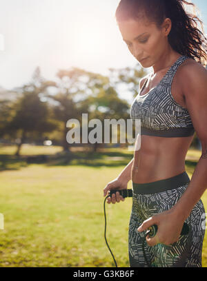 Shot of fitness woman exercising with jump rope in a park. Healthy female doing skipping workout outdoors on a sunny day. Stock Photo