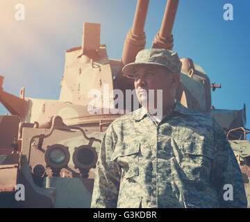 A military soldier is standing in front of an army tank vehicle with sun outside for an american war, defense or security concep Stock Photo