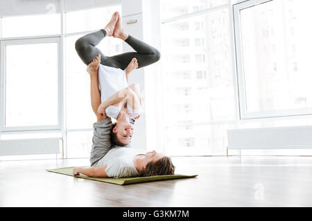 Cheerful young man and woman doing acro yoga in pair in studio Stock Photo