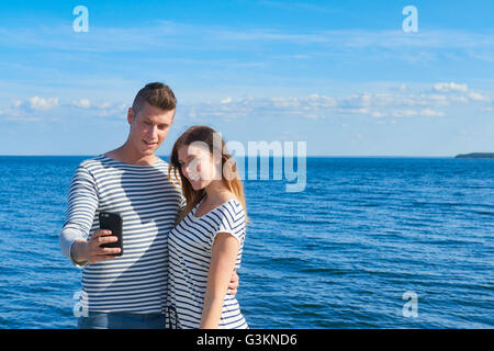 Young couple standing by sea, taking self portrait using smartphone Stock Photo