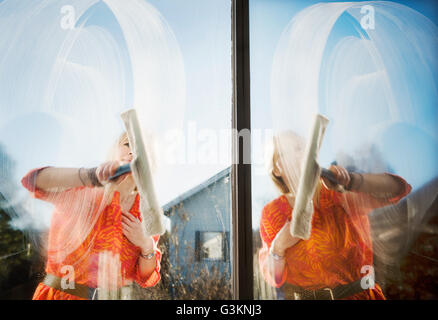 Composite of woman outdoors cleaning windows with squeegee Stock Photo