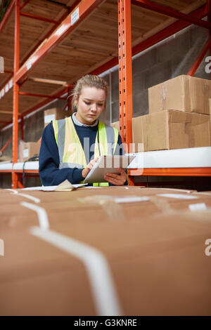 Female factory worker checking package on digital tablet in factory warehouse packing Stock Photo