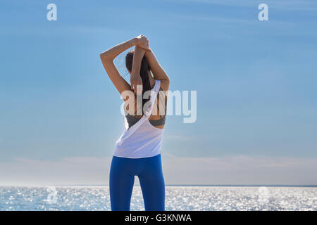 Rear view of young woman arms raised hands behind head stretching Stock Photo