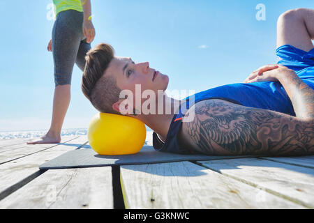 Tattooed man lying on pier using ball as pillow Stock Photo