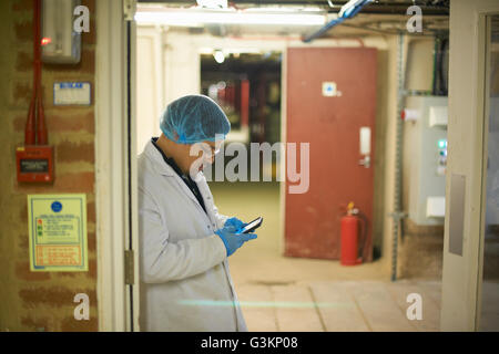 Worker wearing hair and latex gloves leaning against doorway using smartphone Stock Photo
