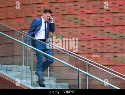 Mature businessman walking down steps, using smartphone Stock Photo