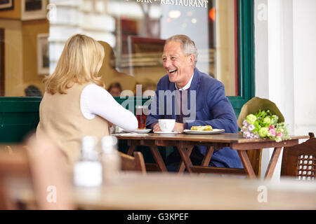 Mature couple on date laughing together at sidewalk cafe table Stock Photo