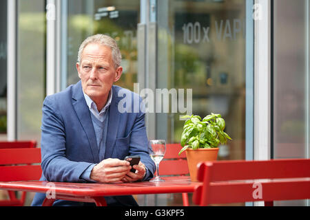 Mature man with smartphone waiting at sidewalk cafe Stock Photo