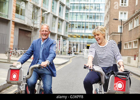 Mature dating couple laughing whilst cycling on hire bicycles, London, UK Stock Photo