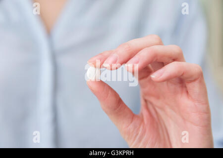 Womans hand holding pill between thumb and forefinger Stock Photo