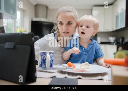 Mother and son sitting at table, looking at digital tablet Stock Photo
