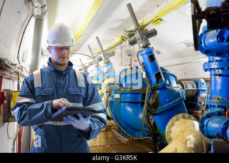 Worker using digital tablet to take readings in straining gallery in hydroelectric power station Stock Photo