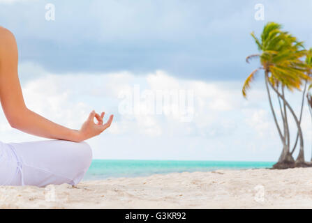 Cropped rear view of young woman practicing yoga lotus pose on beach, Dominican Republic, The Caribbean Stock Photo