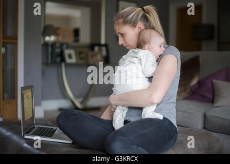Mother holding baby boy whilst using laptop Stock Photo