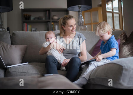 Mother sitting in living room with son and baby boy, son holding digital tablet Stock Photo