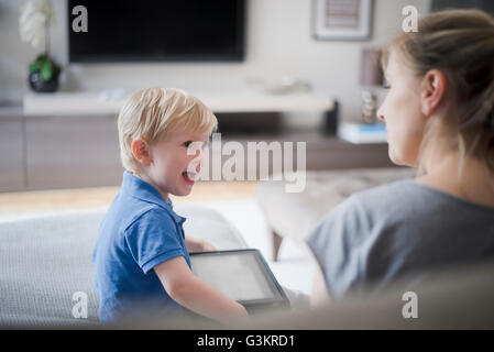 Mother and son sitting together, son holding digital tablet, laughing Stock Photo