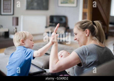 Mother and son giving high five, baby boy asleep on mother's lap Stock Photo