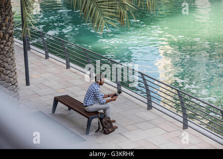 High angle view of young man sitting at waterfront using digital tablet, Dubai, United Arab Emirates Stock Photo