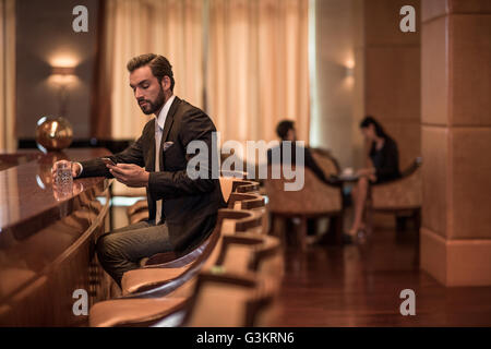 Young businessman sitting at hotel bar reading smartphone texts Stock Photo
