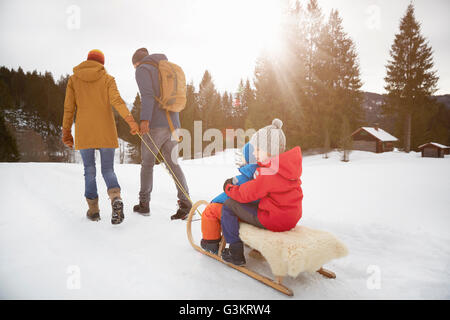 Rear view of parents pulling sons on toboggan in snow landscape, Elmau, Bavaria, Germany Stock Photo