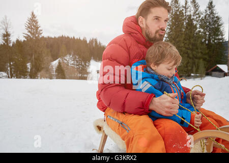 Young man and son tobogganing in snow, Elmau, Bavaria, Germany Stock Photo