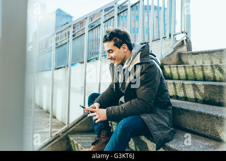 Man sitting on step using smartphone smiling Stock Photo