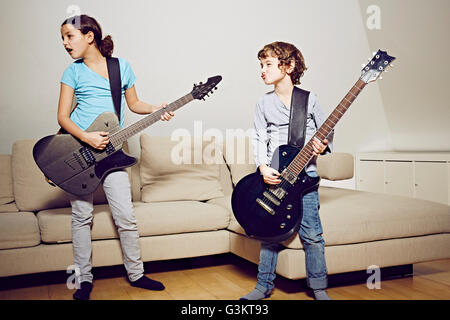 Boy and girl in lounge playing guitars looking away Stock Photo