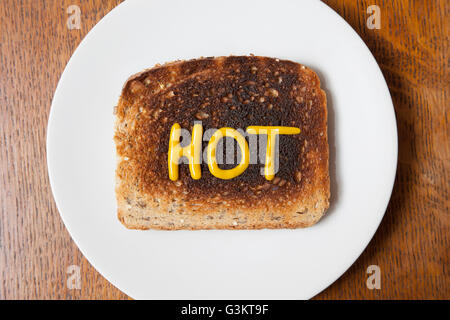 Overhead view of the word hot written in mustard on burnt toast Stock Photo