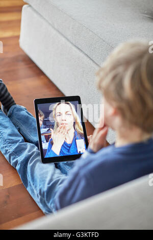 Boy sitting on floor blowing a kiss to mother on digital tablet video call