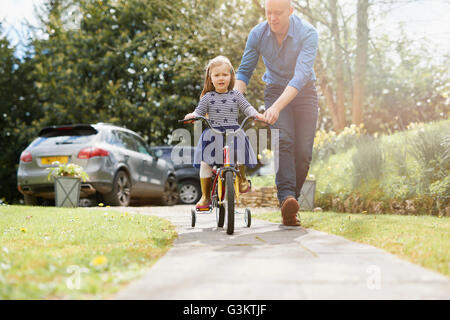 Father teaching daughter to ride bicycle on street Stock Photo