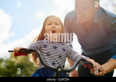 Father teaching daughter to ride bicycle Stock Photo