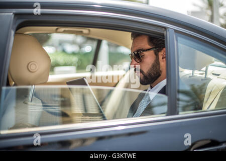 Young businessman using digital tablet in car backseat, Dubai, United Arab Emirates Stock Photo
