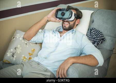 Young man on armchair looking through virtual reality headset Stock Photo