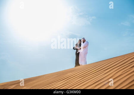 Middle eastern couple wearing traditional clothes taking smartphone selfie on desert dune, Dubai, United Arab Emirates Stock Photo