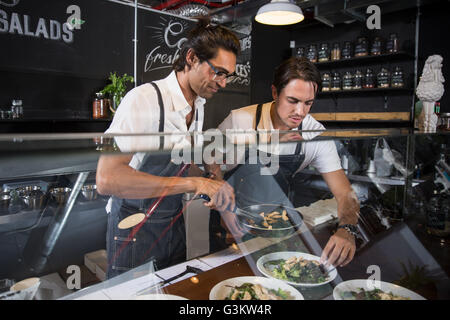 Restaurateurs preparing salad behind service counter Stock Photo