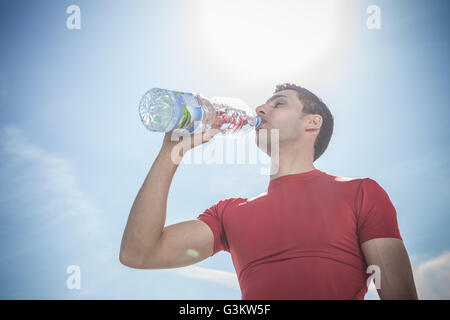 Young man drinking bottled water against blue sky
