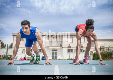 Young male and female sprinters on their marks on running track Stock Photo
