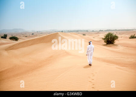 Rear view of young middle eastern man wearing traditional clothes walking in desert, Dubai, United Arab Emirates Stock Photo
