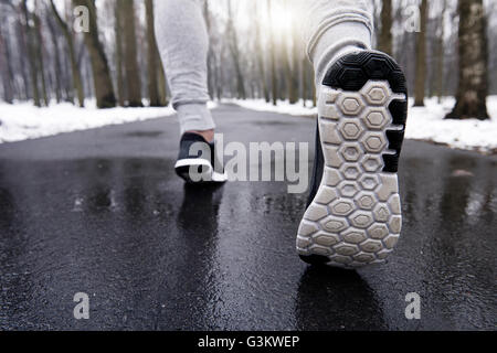 Young man jogging through snowy forest, low section, rear view Stock Photo